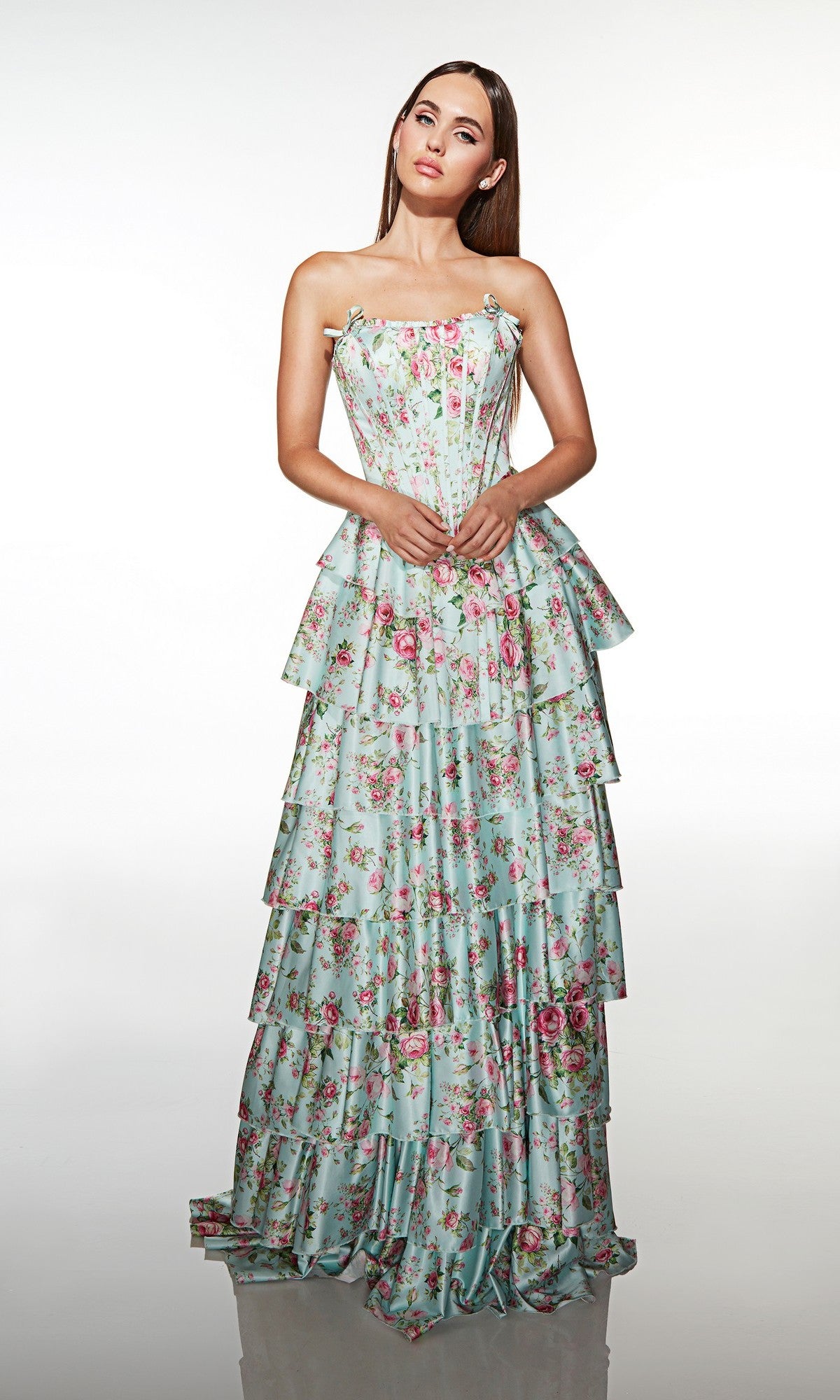 A woman wearing the Alyce 62066 long prom dress, featuring a strapless tiered ruffle skirt with a blue base and pink floral print, stands against a plain white background.